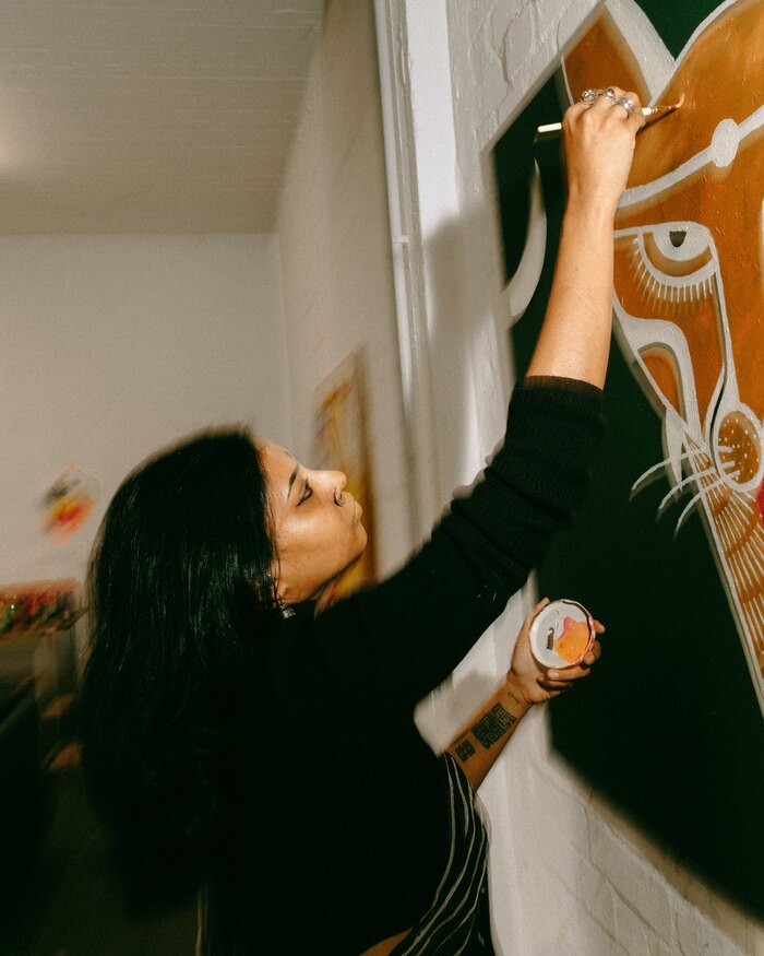 Mugdha Martin reaching up to paint the eye of a tiger on a green canvas