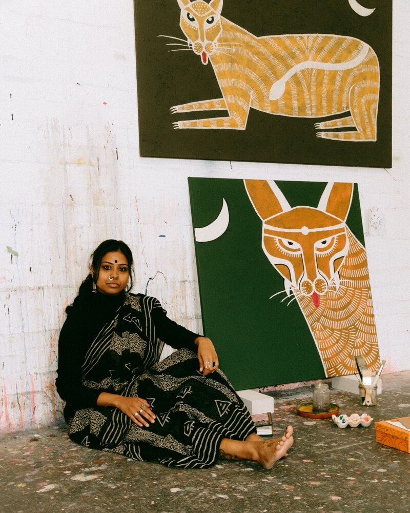 Mugdha Martin sitting on the studio floor beside two Big Cats canvases
